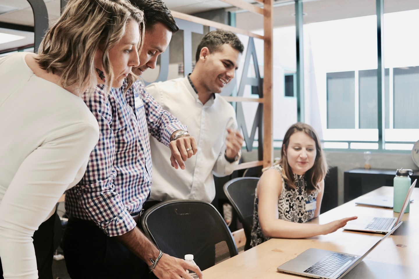 Diverse professionals die samenwerken op laptops aan een lichte houten tafel.